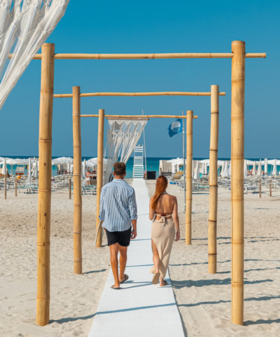 Coppia cammina sulla spiaggia sotto archi di bambù.